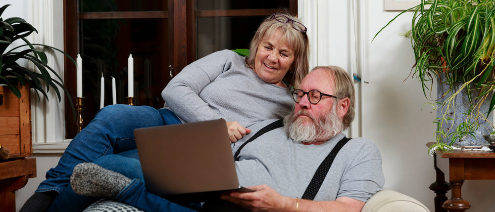 Ett äldre par sitter i soffan och tittar på en laptop tillsammans