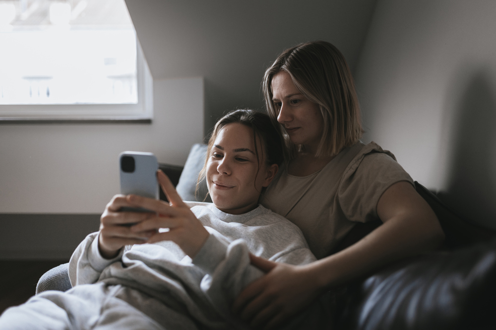 Två kvinnor sitter i en soffa och tittar på en mobiltelefon