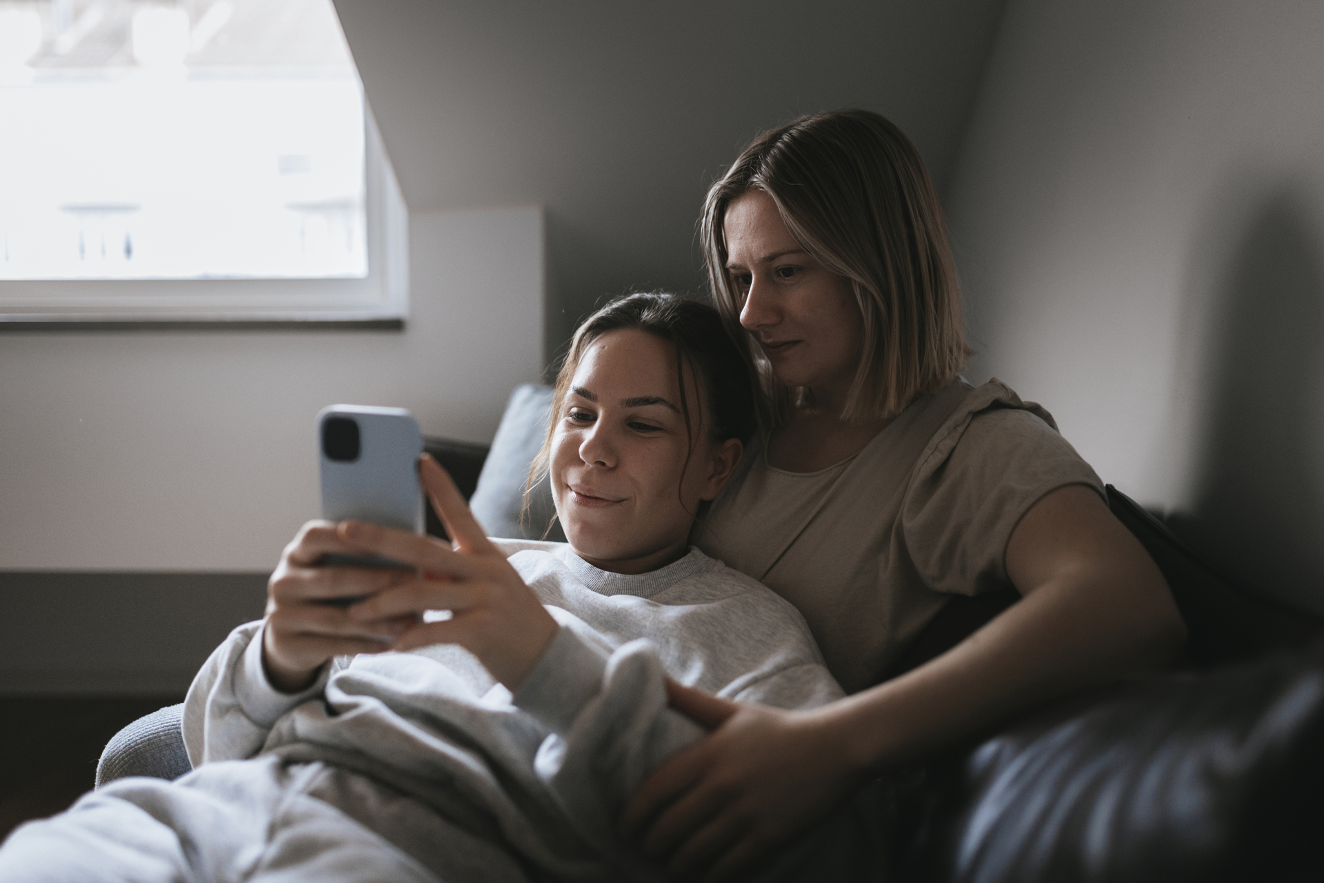Två kvinnor sitter i en soffa och tittar på en mobiltelefon
